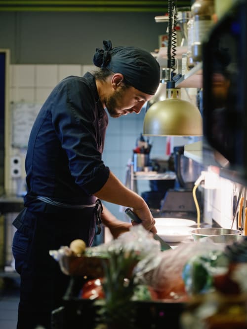 Chef en préparation d'un plat à la cuisine de l'Hôtel De La Sage avec des ingrédients frais et un équipement professionnel