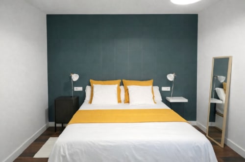 Moderno dormitorio en Living Sur con cabecera azul teal, ropa de cama amarilla, almohadas blancas y decoración minimalista en Sanlúcar de Barrameda