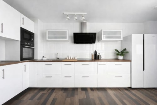 Cocina moderna blanca con encimeras de madera, electrodomésticos negros y campana extractora de acero inoxidable en apartamento Living Sur
