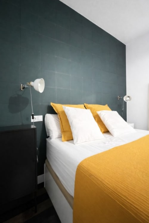 Dormitorio moderno en Living Sur Sanlúcar con pared de acento verde oscuro, ropa de cama blanca, mantas amarillas e iluminación ajustable