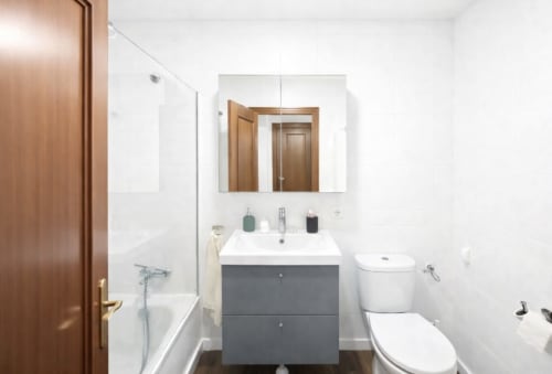 Baño moderno en apartamento Living Sur, Sanlúcar de Barrameda, con azulejos blancos tipo metro, tocador gris, espejo de botiquín y inodoro