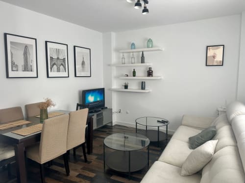 Sala de estar moderna en apartamento Solera y Mar con sofá, comedor, TV, estantes flotantes y arte mural arquitectónico
