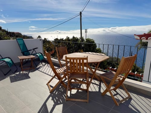 Sunny terrace at Check Madeira hotel in Ribeira Brava with wooden dining table, chairs, and ocean view