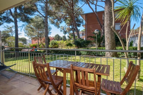 Ground floor apartment terrace with wooden dining table and chairs overlooking lush gardens in Palafrugell