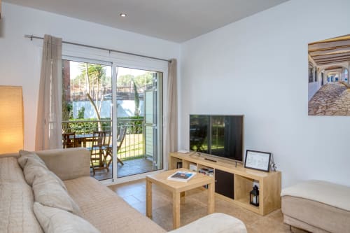 Bright apartment living room in Palafrugell with garden view, flat-screen TV, wooden furniture, and glass doors opening to