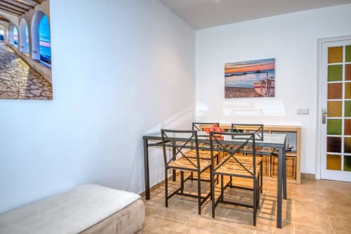 Modern dining area in Palafrugell apartment with black metal table, wooden chairs, beach sunset artwork, and garden views