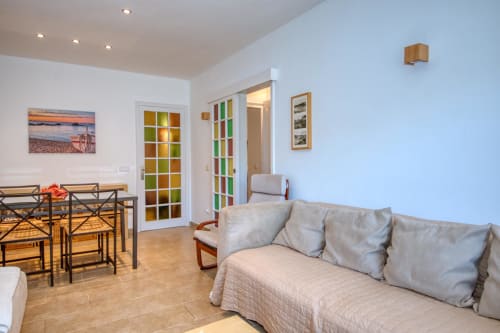 Bright apartment living area in Palafrugell with sofa, dining table, colorful glass doors, and wooden furnishings