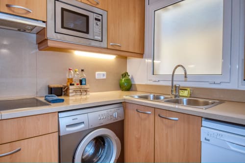 Modern kitchen in Palafrugell apartment with wooden cabinets, stainless steel appliances, microwave, washing machine, and