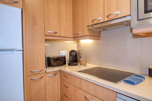 Modern kitchen in Palafrugell apartment with wooden cabinets, stainless steel cooktop, and built-in appliances