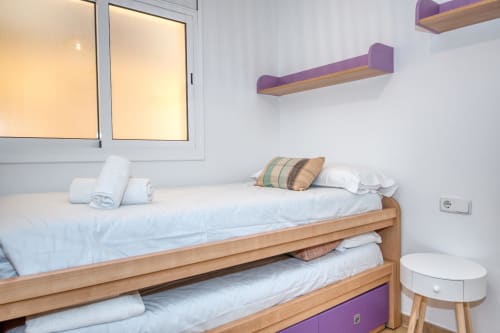 Bright bedroom with bunk bed, wooden frame, purple accents, and white bedding at Finques Garcia Enrich apartment in