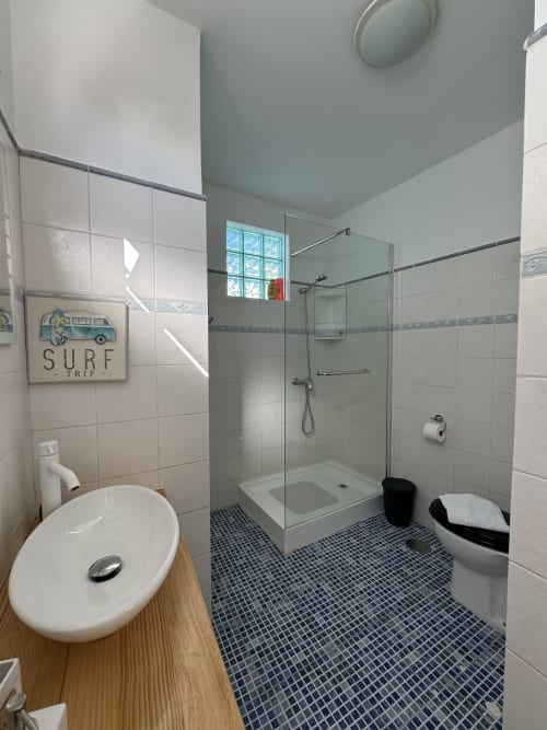 Modern bathroom at Check Madeira with glass shower, round sink, blue mosaic floor tiles, and surf trip wall decor