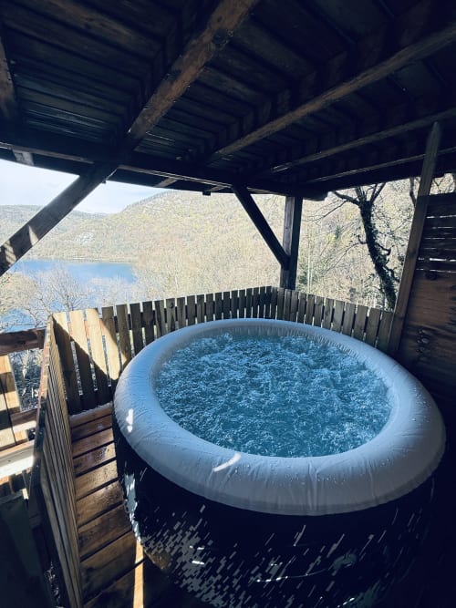 Vasca idromassaggio riscaldata all'aperto su terrazza in legno con vista sul lago e sulle montagne presso la villa Cabane LA CHENAIE a Serrières-sur-Ain
