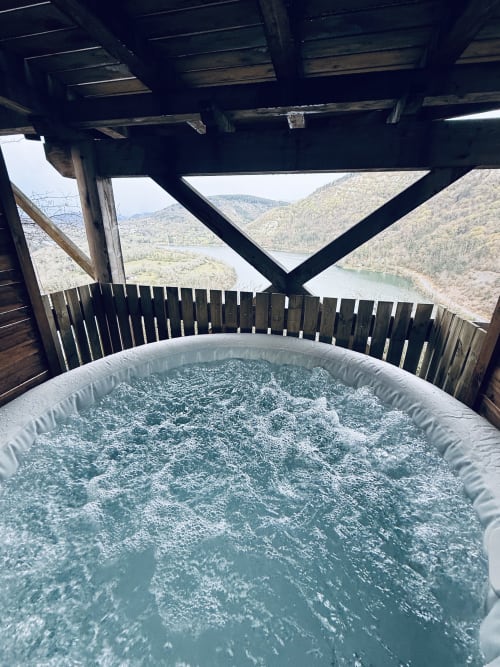 Vasca idromassaggio frizzante su terrazza in legno con vista sul Lago del Genin e montagne boscose alle Cabane del Belvedere, Serrières-sur-Ain