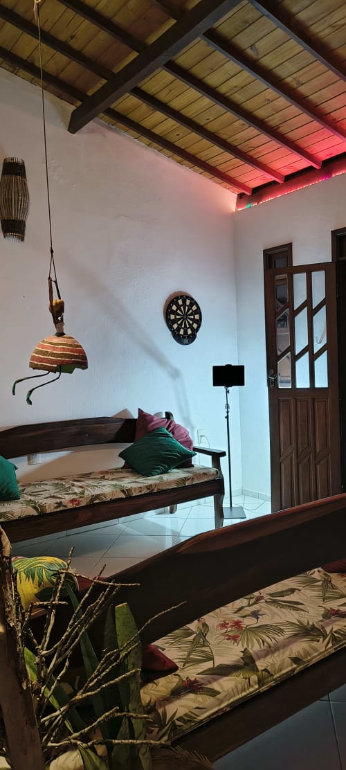 Quarto rústico na Casa do Porto com vigas de madeira, alvo de dardos, luminária suspensa e roupa de cama estampada em Boipeba, Brasil