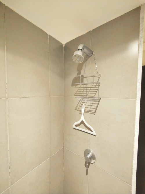 Rincón de ducha con accesorios cromados, canastas de almacenaje y perchero blanco en apartamento de Ciudad de México