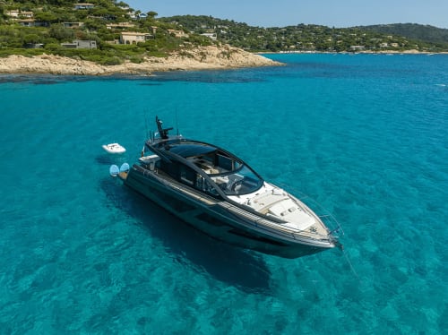 Luxury yacht anchored in turquoise waters off Saint Florent, Corsica, with coastal cliffs and villas visible