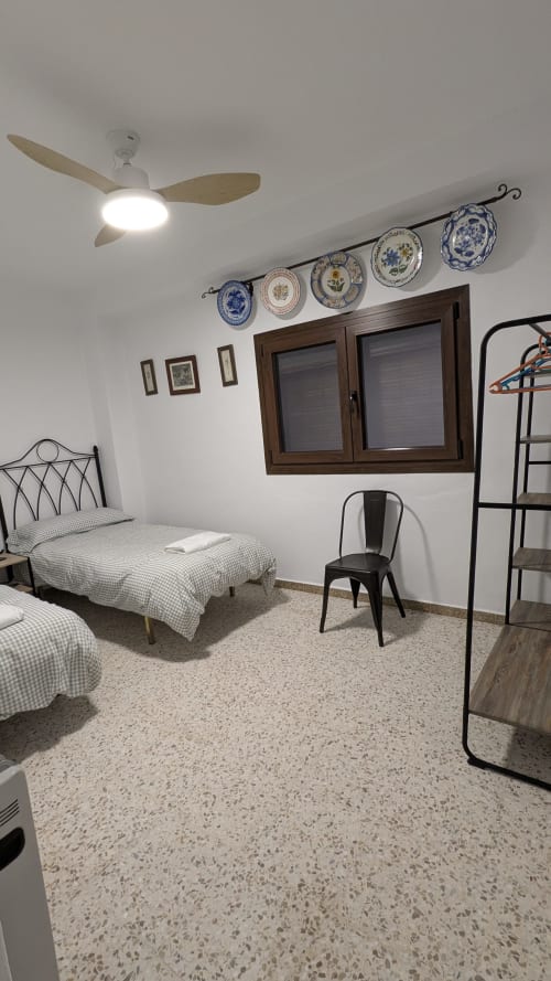 Dormitorio de villa rústica en Salteras con camas gemelas, estantería decorativa, ventilador de techo, ventana de madera y piso de terrazo