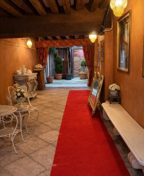 Elegant hallway at Palazzo Titti Venice with red carpet, ornate decor, and courtyard view