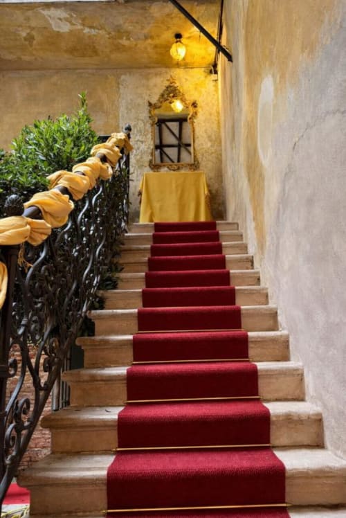 Elegant staircase with red carpet runner at Palazzo Titti Venice, ornate iron railing and warm lighting
