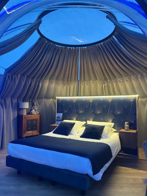 Chambre bulle transparente à l'hôtel Bubble Jade avec lit queen, tête de lit motifée et éclairage bleu sous un ciel étoilé