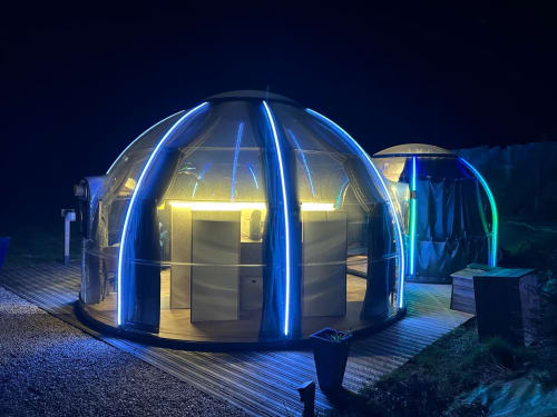 La bulle transparente illuminée de Bubble Jade la nuit, liseré néon bleu, terrasse en bois et jacuzzi privé à Bazouges