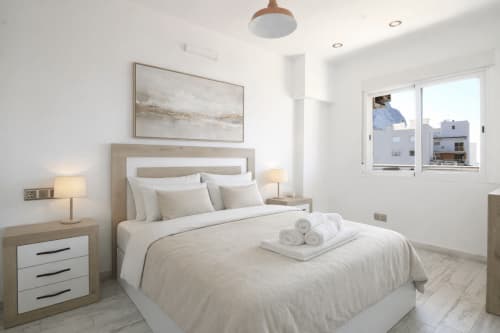 Modern bedroom with sea view in Riurau Home apartment, Calpe. Neutral bedding, wooden furniture, balcony overlooking