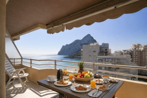 Beachfront balcony breakfast setup at Riurau Home Calpe with sea view, fruit, pastries and mountain backdrop