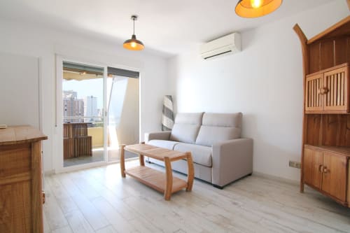 Bright modern apartment living room at Riurau Home Calpe with gray sofa, wooden furniture, sea view balcony, and city skyline