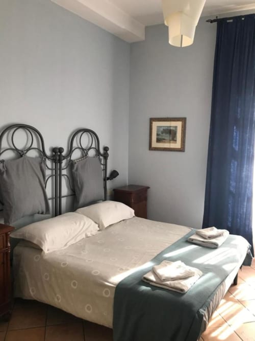 Camera presso l'Affittacamere Numero3 a Cagliari con letto in ferro battuto, biancheria bianca e tende blu