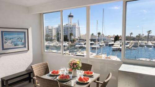 Comedor con vistas al puerto en Holidays Costa Brava, Empuriabrava. Mesa servida con sandía, frente a veleros amarrados