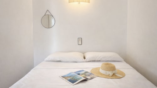 Dormitorio luminoso y minimalista en Holidays Costa Brava con ropa de cama blanca, sombrero de paja y revistas de viajes en Empuriabrava