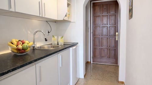 Cocina moderna con armarios blancos, encimera oscura y frutero en apartamento de Empuriabrava