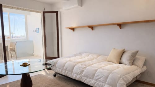 Dormitorio moderno en Holidays Costa Brava con cama blanca, estantería de madera y vistas al canal desde el balcón en Empuriabrava