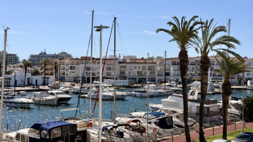Marina de Empuriabrava con veleros, palmeras y apartamentos frente al mar en Holidays Costa Brava