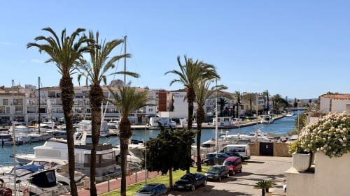 Vista de la marina de Empuriabrava con barcos amarrados, palmeras y arquitectura mediterránea frente al mar