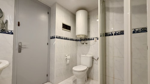 Baño moderno en Holidays Costa Brava con azulejos blancos, cenefa decorativa, mampara de ducha, inodoro, calentador de agua y
