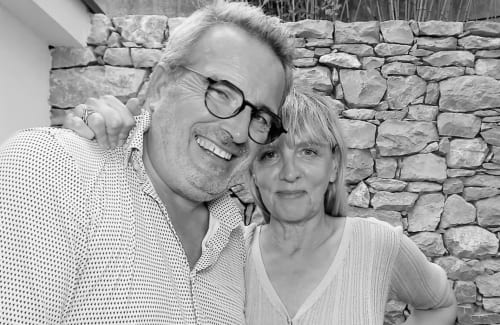 Couple souriant à La Maison du Potier, gîte à Valras-Plage, avec mur en pierre en arrière-plan