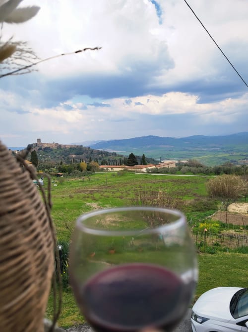 Bicchiere di vino rosso con vista sulla campagna di Montecatini Val di Cecina, Italia, con antico borgo collinare e dolci colline verdi