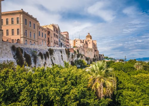 Centro storico di Cagliari con edifici storici color pastello su scogliere che dominano la vegetazione verde e la costa mediterranea