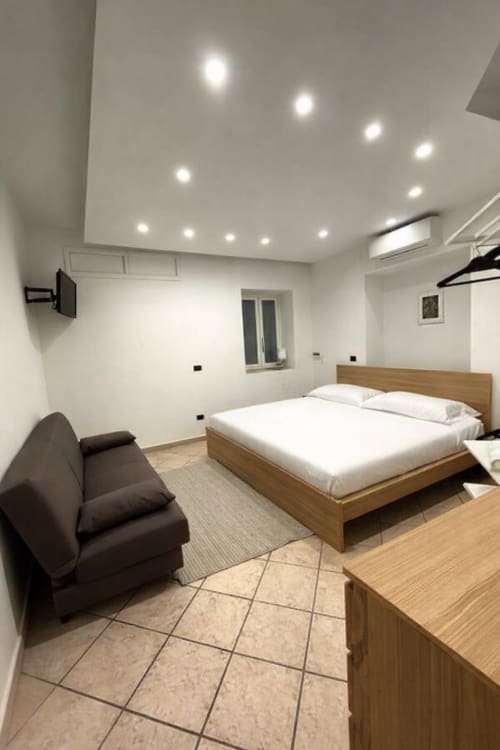 Modern bedroom at SambaSStays Carioca apartment in Cataldo with wooden bed, sofa, recessed ceiling lights, and kitchenette