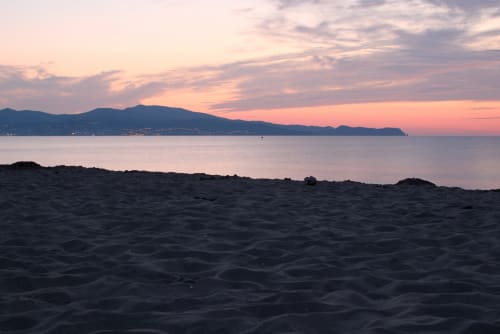 Vista del atardecer desde la playa de Sant Pere Pescador con montañas perfiladas al otro lado de la bahía