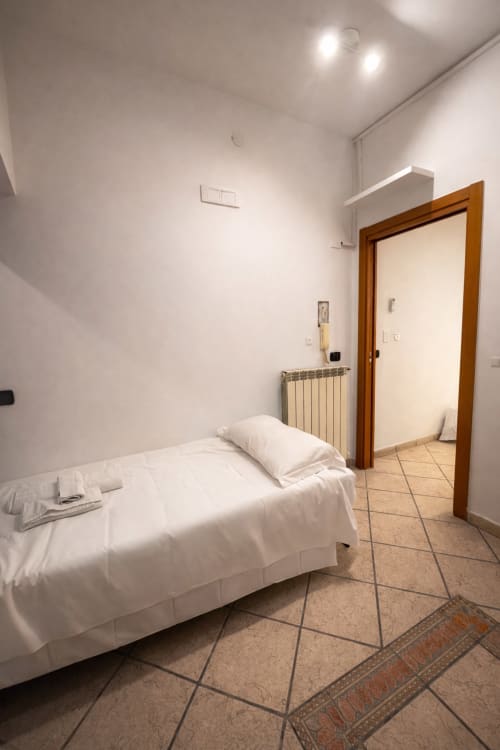 Bright, minimalist bedroom at SambaSStays Carioca Bilocale in Cataldo with white bed, wooden door, and terracotta tile
