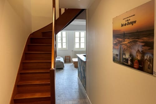 Escalier en bois dans le couloir d'un appartement breton, menant à un séjour meublé avec vue sur la ville