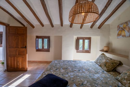 Amplia habitación del Hotel Spa El Batán con vigas de madera expuestas, lámpara de techo tejida y vistas al río