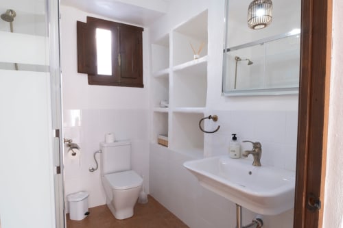 Baño luminoso en Casita del Río 1 del Hotel Spa El Batán con azulejos blancos, lavamanos, inodoro, espejo y zona de ducha en Castillo