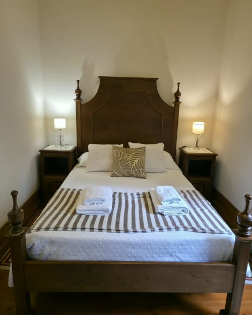 Quarto elegante no Enjoy The North, Viana do Castelo, com cama de madeira com dossel branco e mesas laterais
