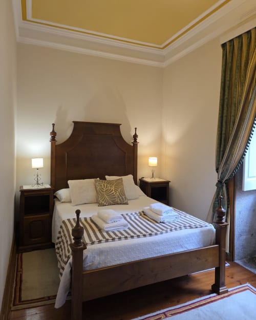 Quarto elegante do hotel Enjoy The North em Viana do Castelo com cama de dossel em madeira, roupa de cama creme e detalhes dourados