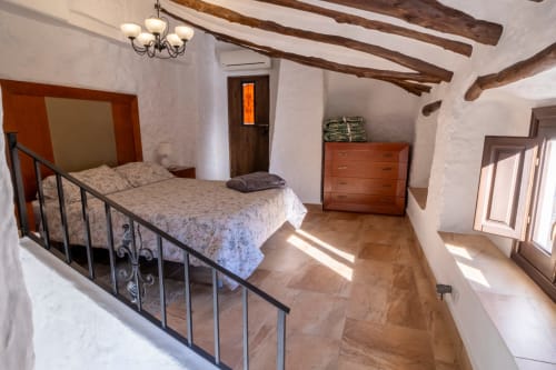 Dormitorio rústico con vigas expuestas en El Batán Hotel Spa, cama de hierro forjado, cómoda de madera y pisos de terracota