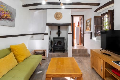 Acogedor salón de apartamento en El Batán Hotel Spa con sofá verde, vigas de madera, chimenea y TV en Castillo de Locubín