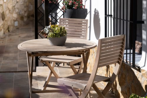 Terraza soleada del Hotel Spa El Batán con mesa de madera, sillas y flores en macetas con vistas al río en Castillo de